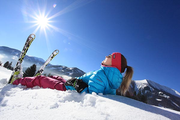 Eine Skifahrerin liegt auf der Skipiste und genießt den strahlenden Sonnenschein.